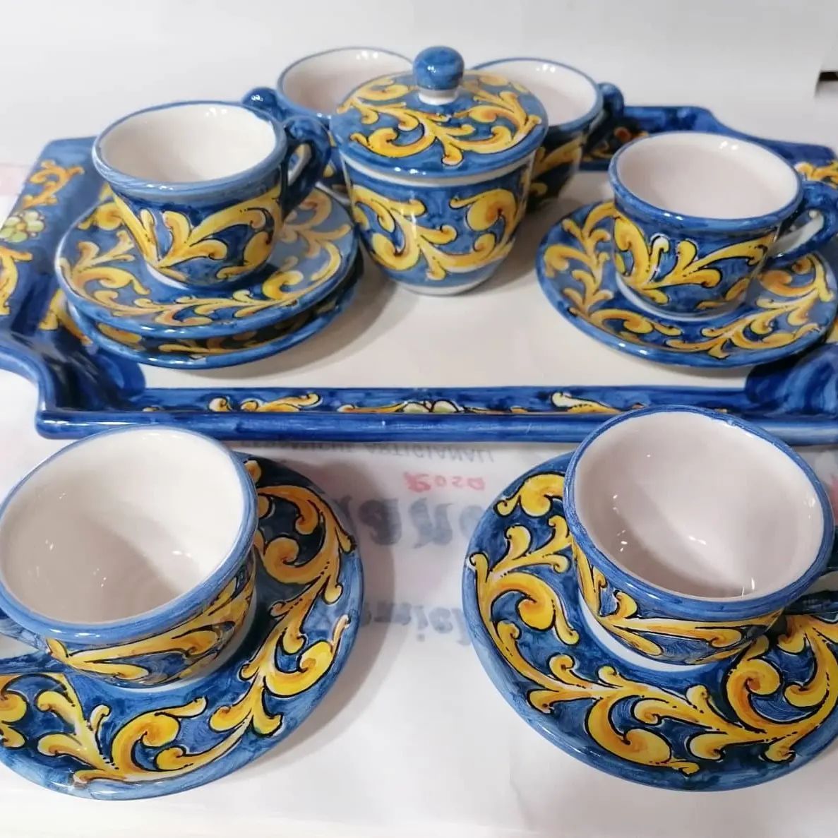 Set da caffè espresso in ceramica blu e gialla su vassoio. Include tazze, piattini e zuccheriera.
