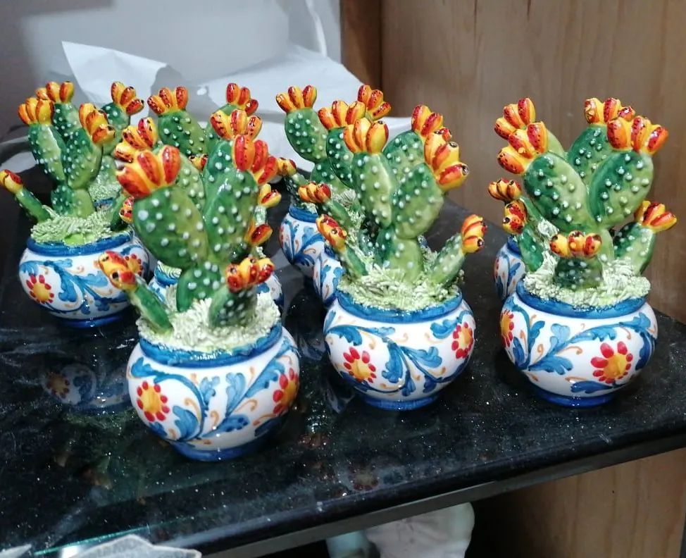 Sculture di cactus con fiori arancioni in vasi di ceramica decorati in blu e bianco, disposti su una superficie nera.
