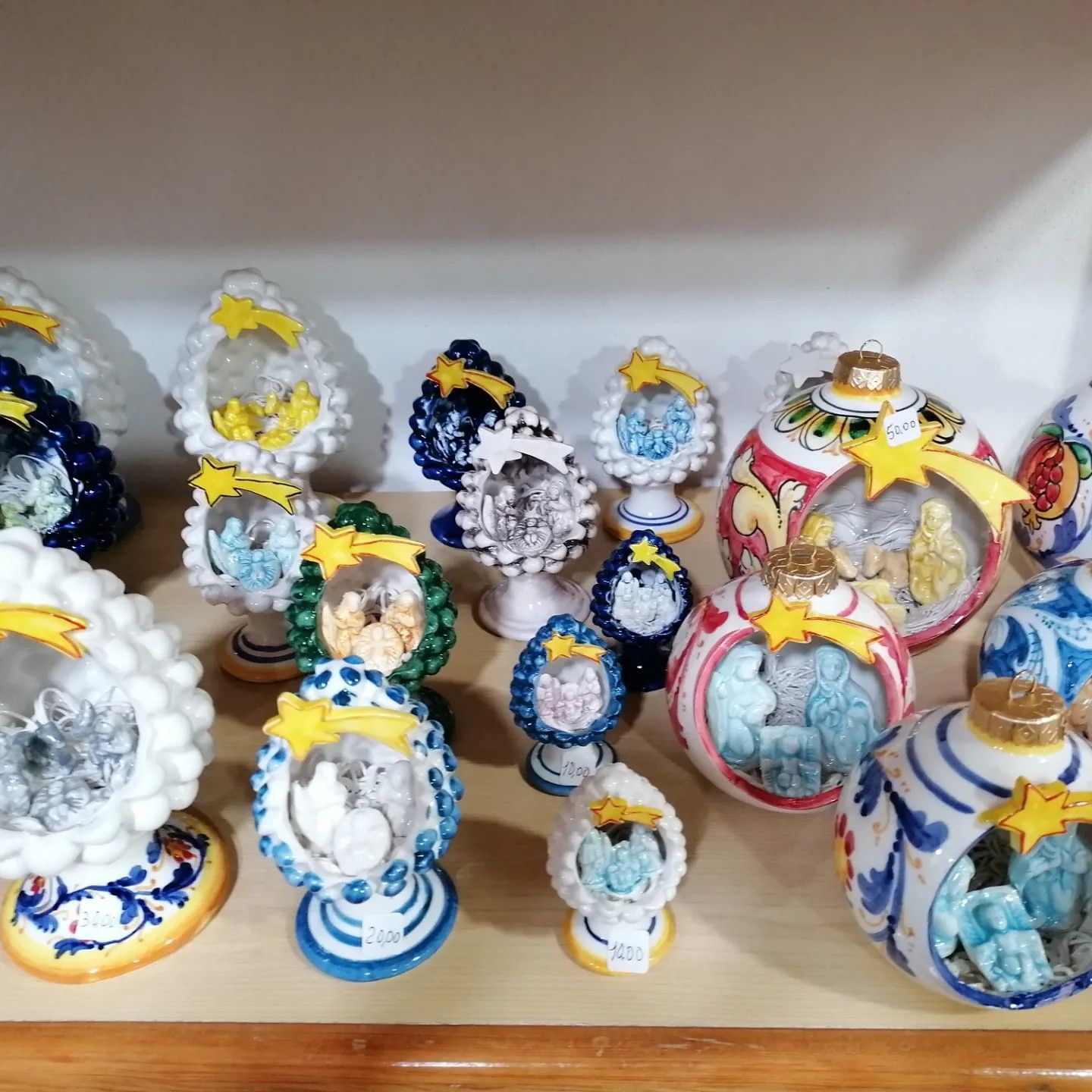 Decorazioni in ceramica per presepe su una mensola. A forma di uovo e di palla, di vari colori, con stelle in cima.