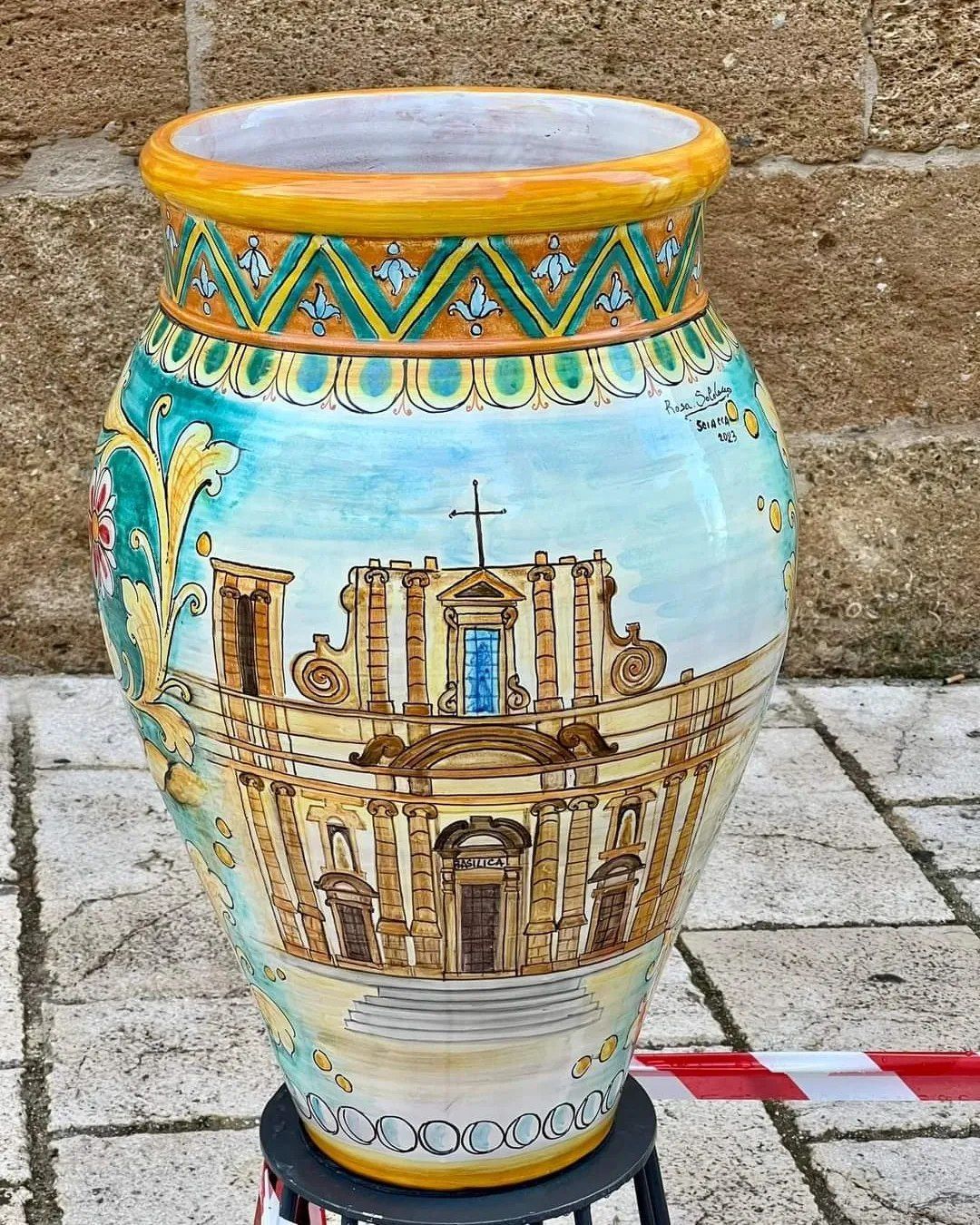 Grande vaso in ceramica decorato e dipinto a mano, raffigurante la facciata di un edificio, con accenti turchesi e gialli.