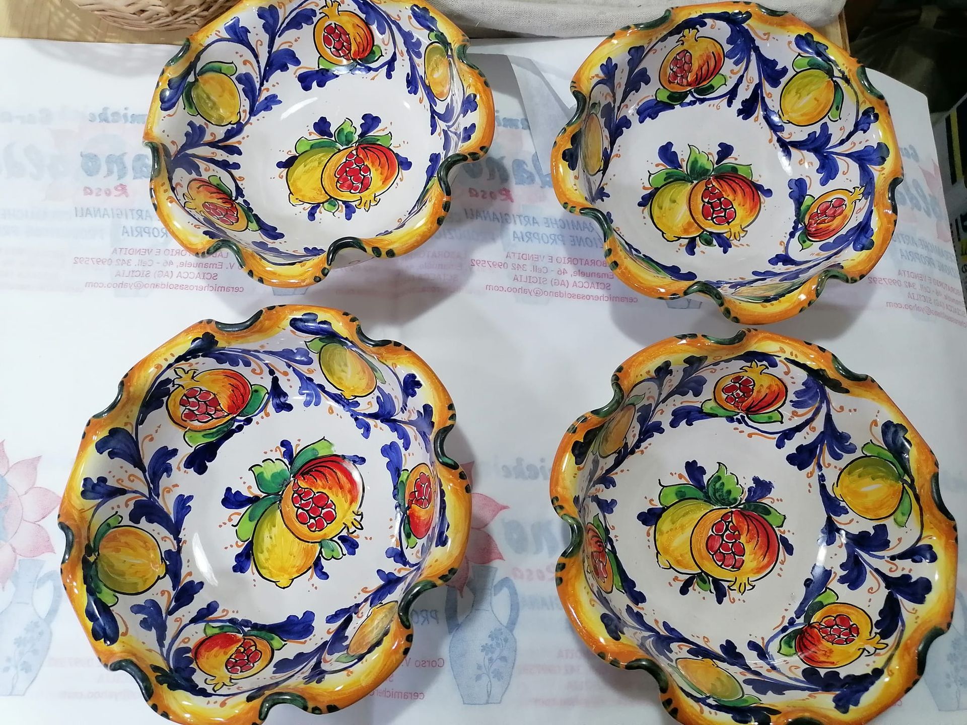 Quattro ciotole in ceramica decorata con motivi di limoni e melograni, dettagli blu e gialli, bordi smerlati.