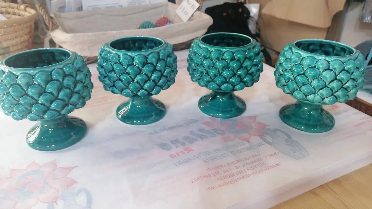 Quattro portacandele in ceramica color verde acqua a forma di carciofo su una superficie bianca.