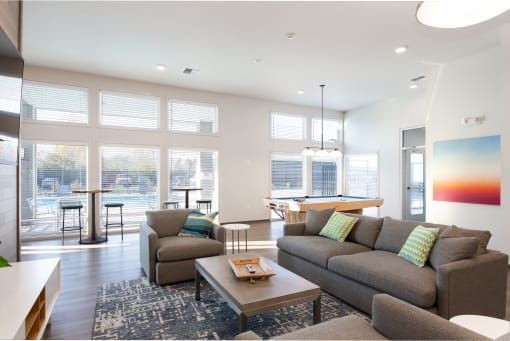 Cozy lounge area with pool view: grey sofa, armchairs, coffee table, pool table, art, large windows.