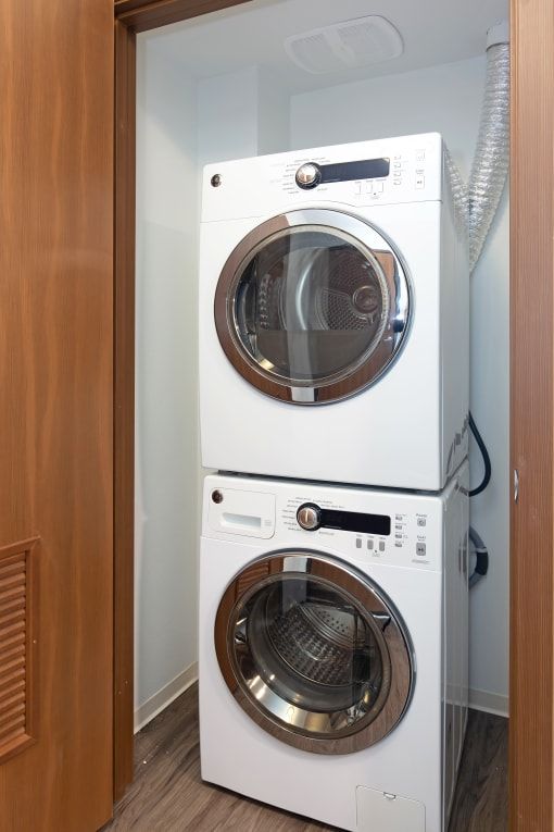Stacked white washer and dryer unit in a small closet.