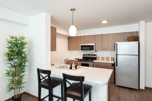 Modern kitchen with white countertops, stainless steel appliances, and two black bar stools.