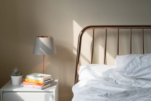 Bedside table with lamp, books, and succulent next to unmade bed with light shining on it.