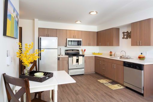 Modern kitchen with wood cabinets, stainless steel appliances, and a white table with yellow flowers.