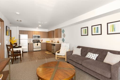 Cozy apartment living space: kitchen, living room with sofa, dining table, hardwood-look floors, neutral colors.