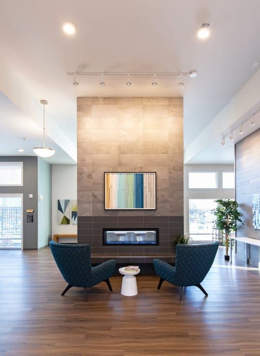 Two teal armchairs face fireplace with art; wood floors and a modern setting.