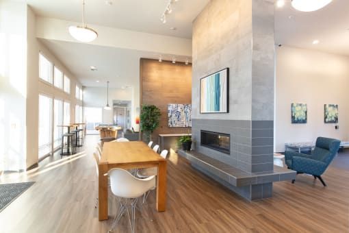 Modern lobby with fireplace, dining table, and seating area. Sunlight streams in from a window.
