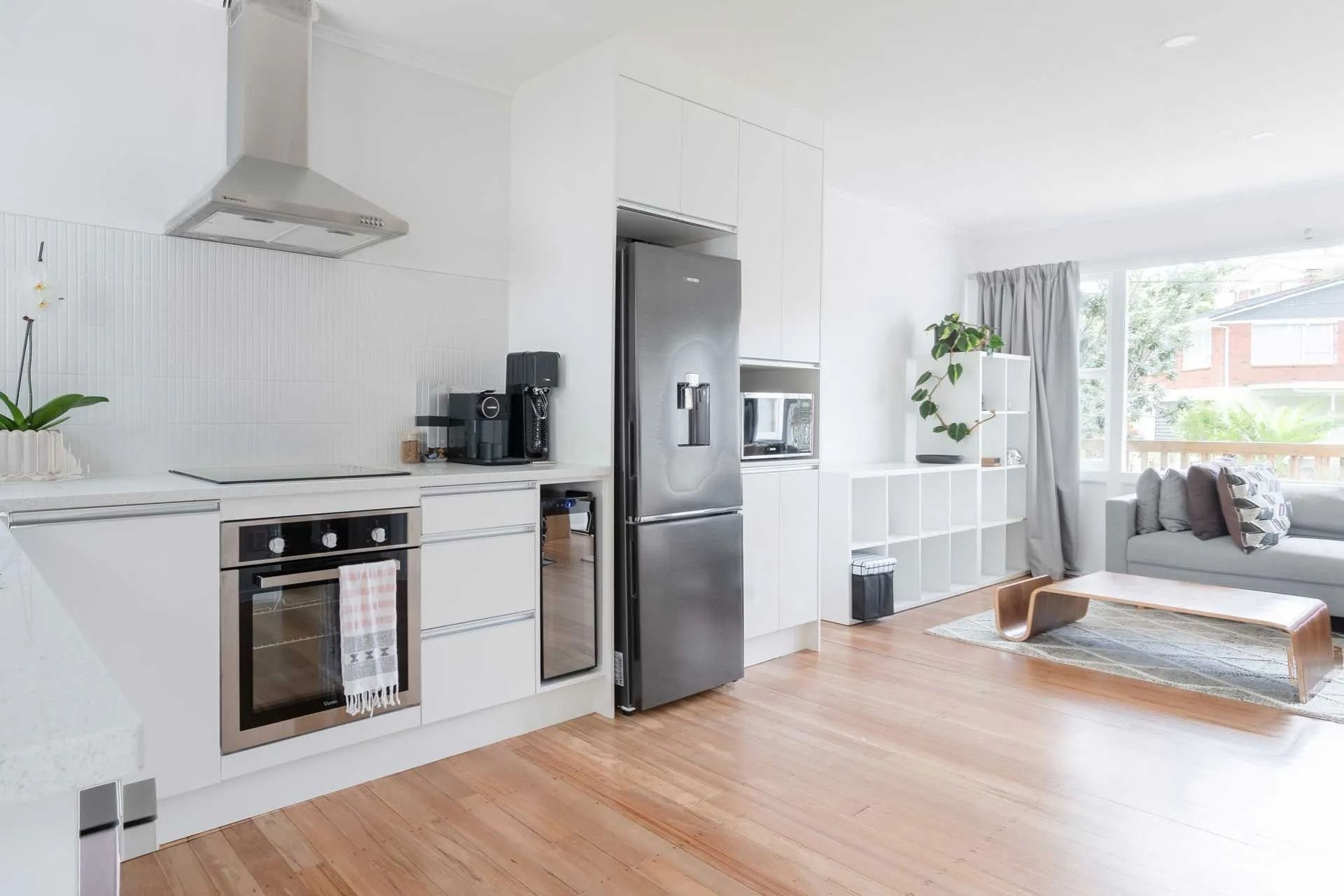 Bright white kitchen with stainless steel appliances, open to a living area with wood floors. Bright white kitchen with stainless steel appliances, open to a living area with wood floors.