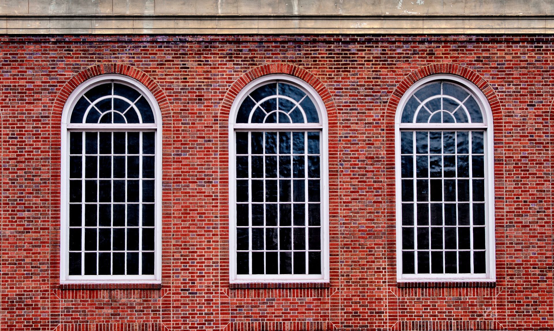 Three arched windows are on the side of a brick building.