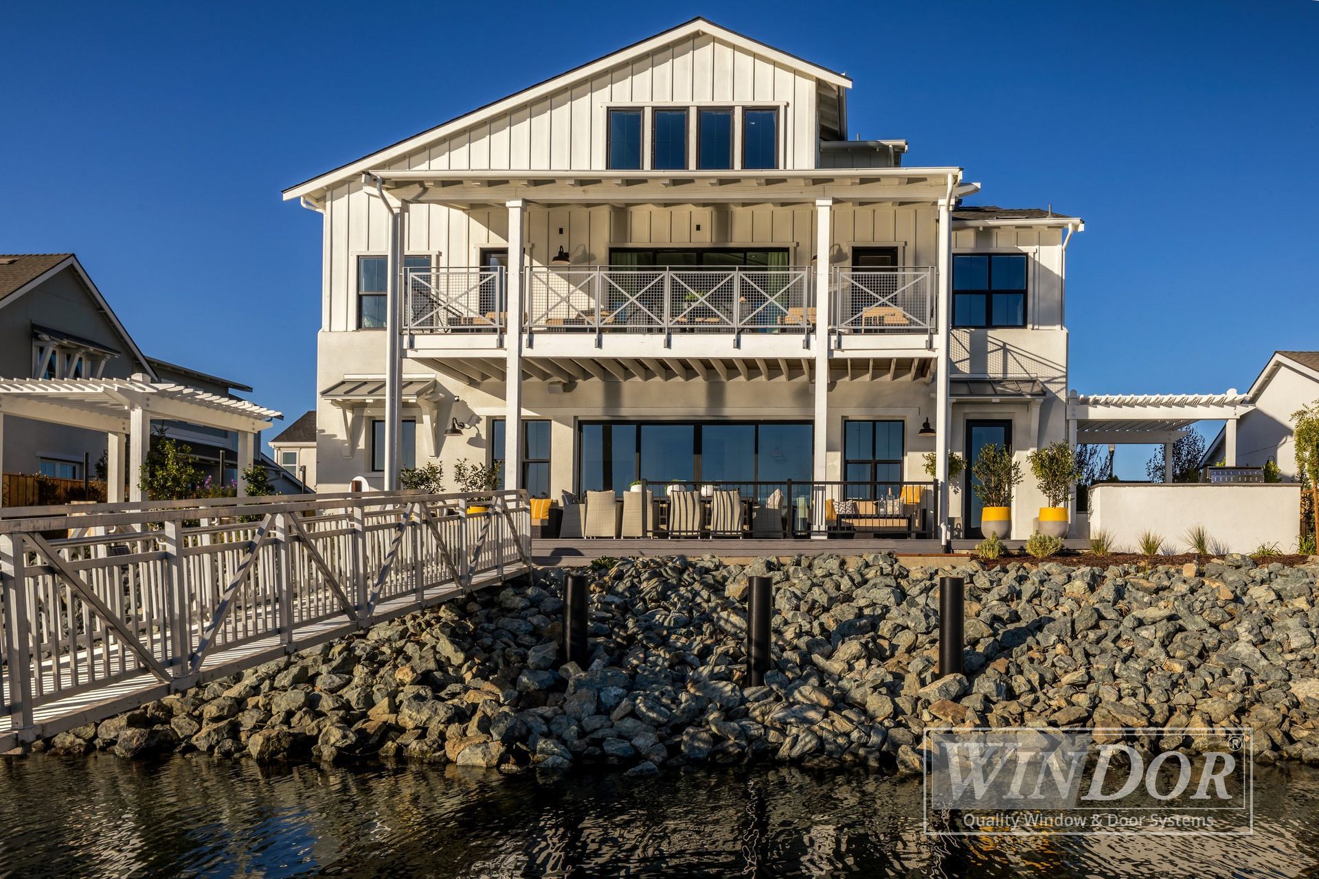 A large white house is sitting on top of a rocky hill next to a body of water.
