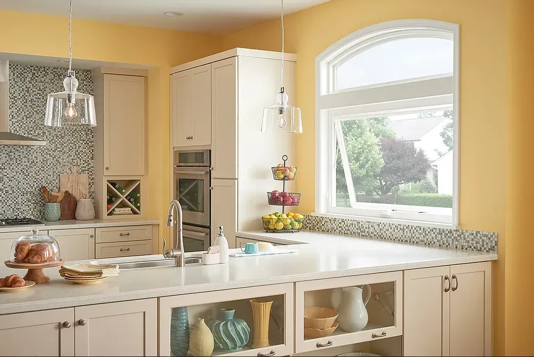 A kitchen with yellow walls and white cabinets and a large window.