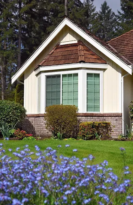 A house with a bay window and purple flowers in front of it.