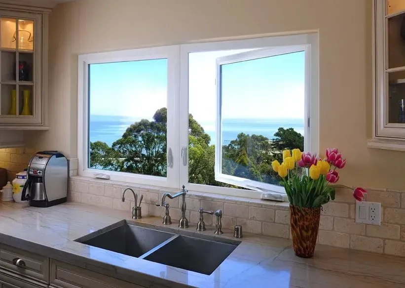 A kitchen with a sink and two windows with a view of the ocean.
