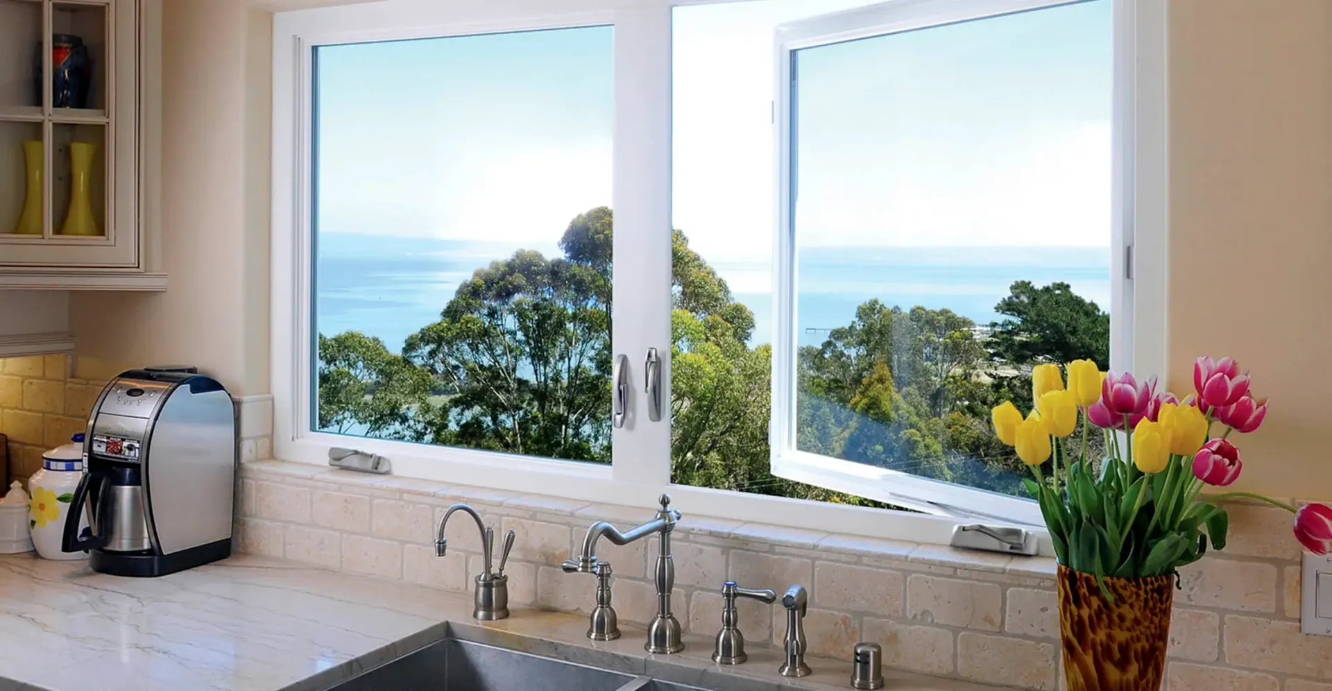 A kitchen with a sink and two windows with a view of the ocean.