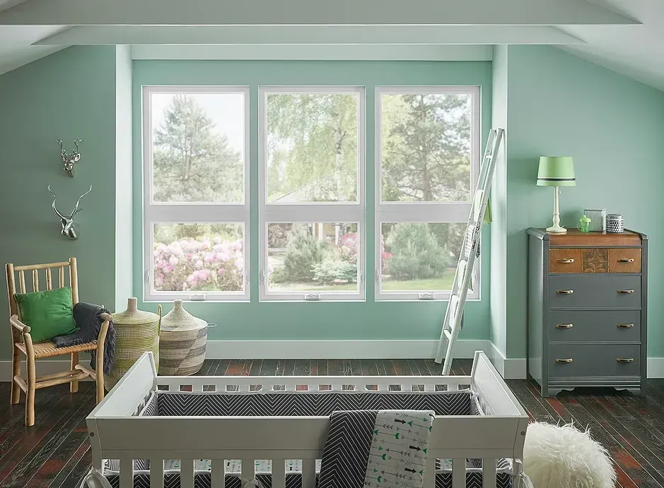 A baby room with green walls and a crib in front of a window.