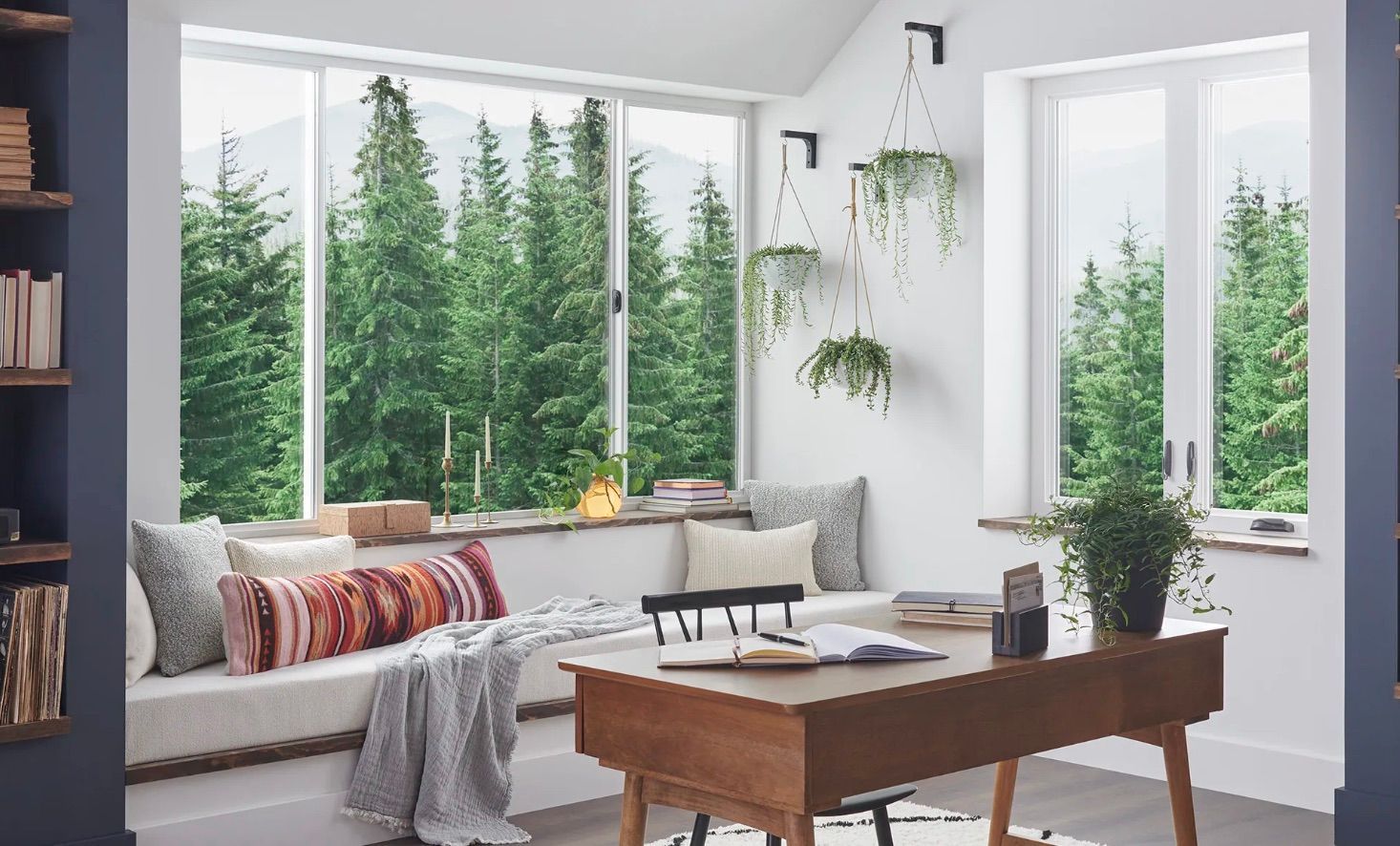 A living room with a desk and a large window with trees in the background.