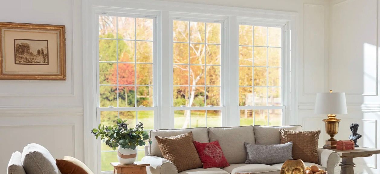 A living room with a couch , table , lamp and lots of windows.