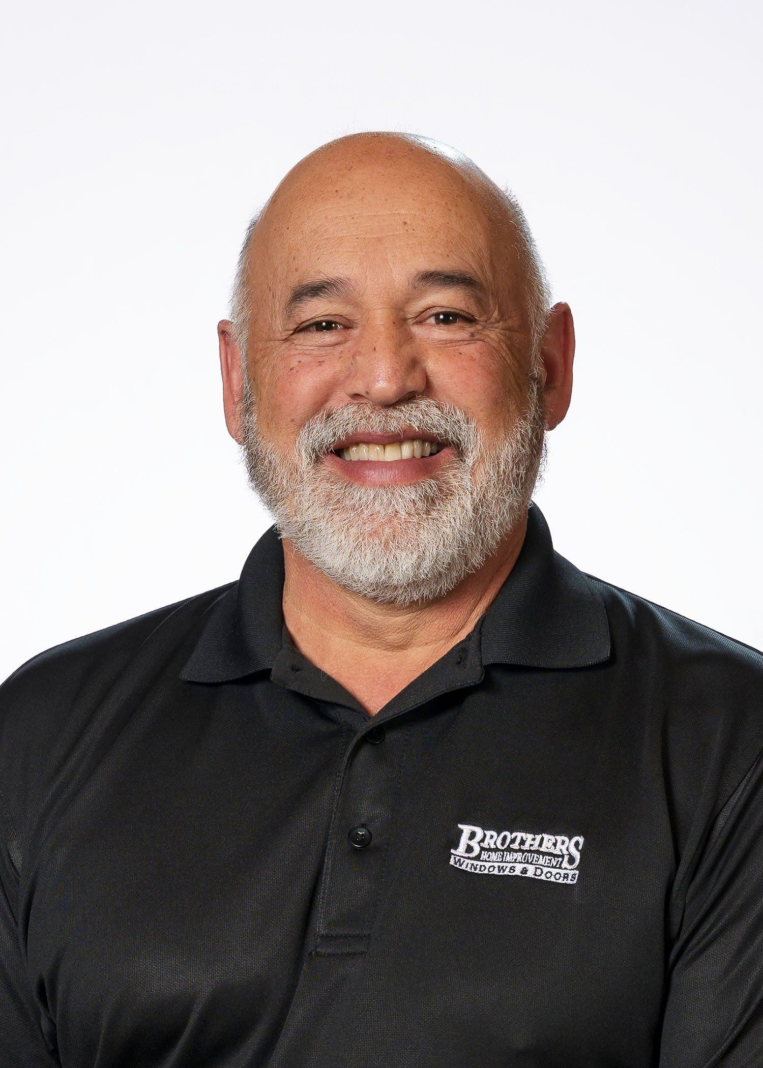 A bald man with a beard is wearing a black polo shirt and smiling.