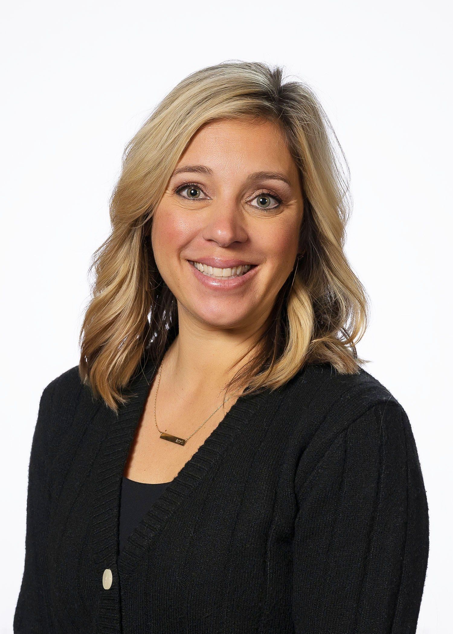 A woman wearing a black sweater and a necklace is smiling for the camera.