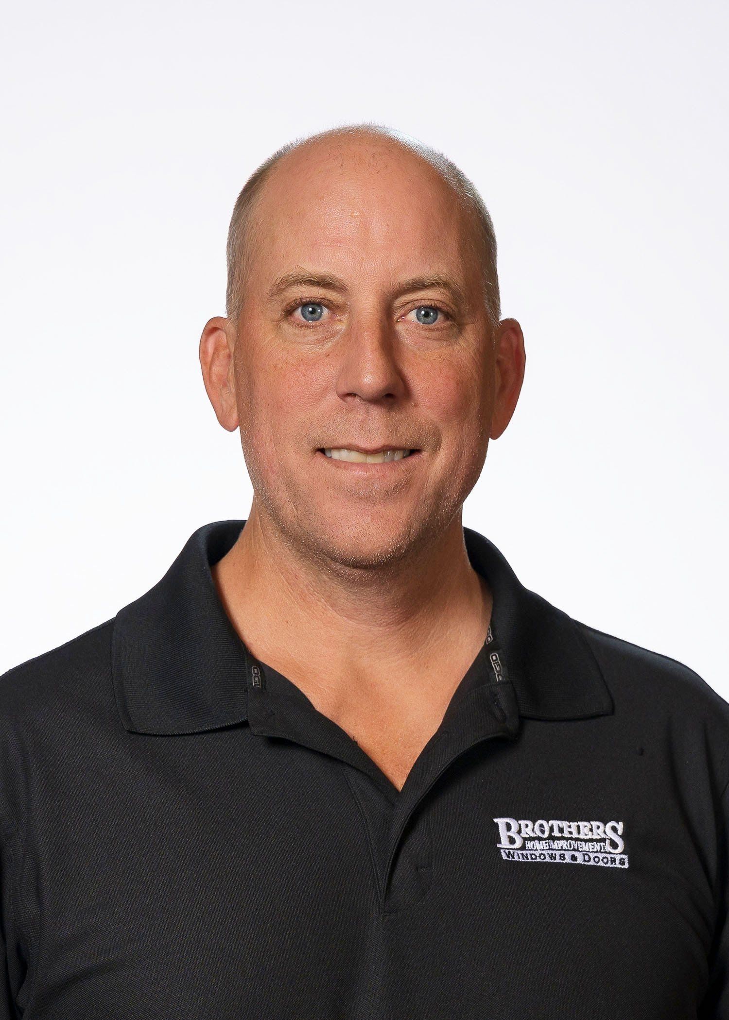 A bald man wearing a black polo shirt is smiling for the camera.