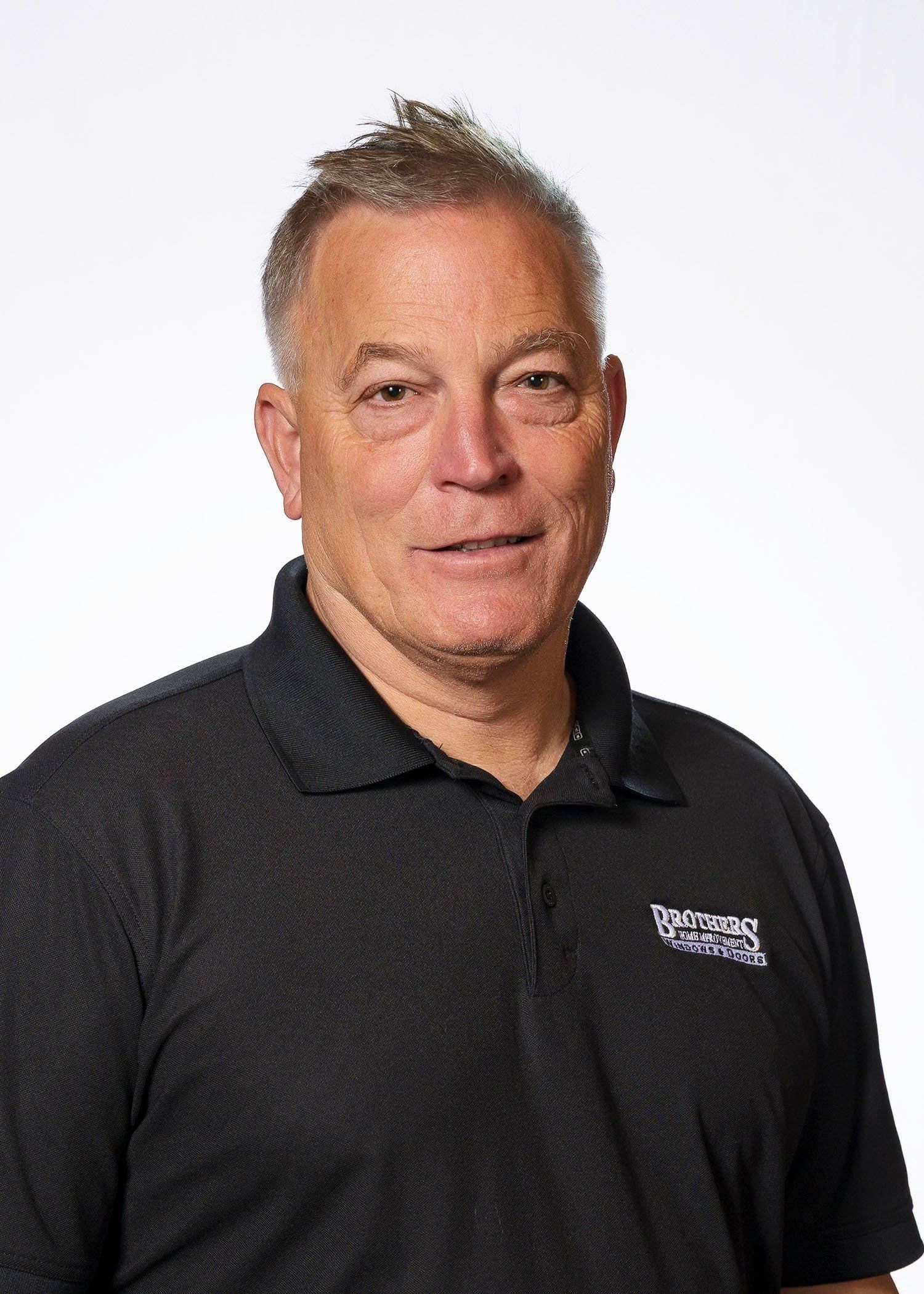 A man in a black shirt is standing in front of a white background.
