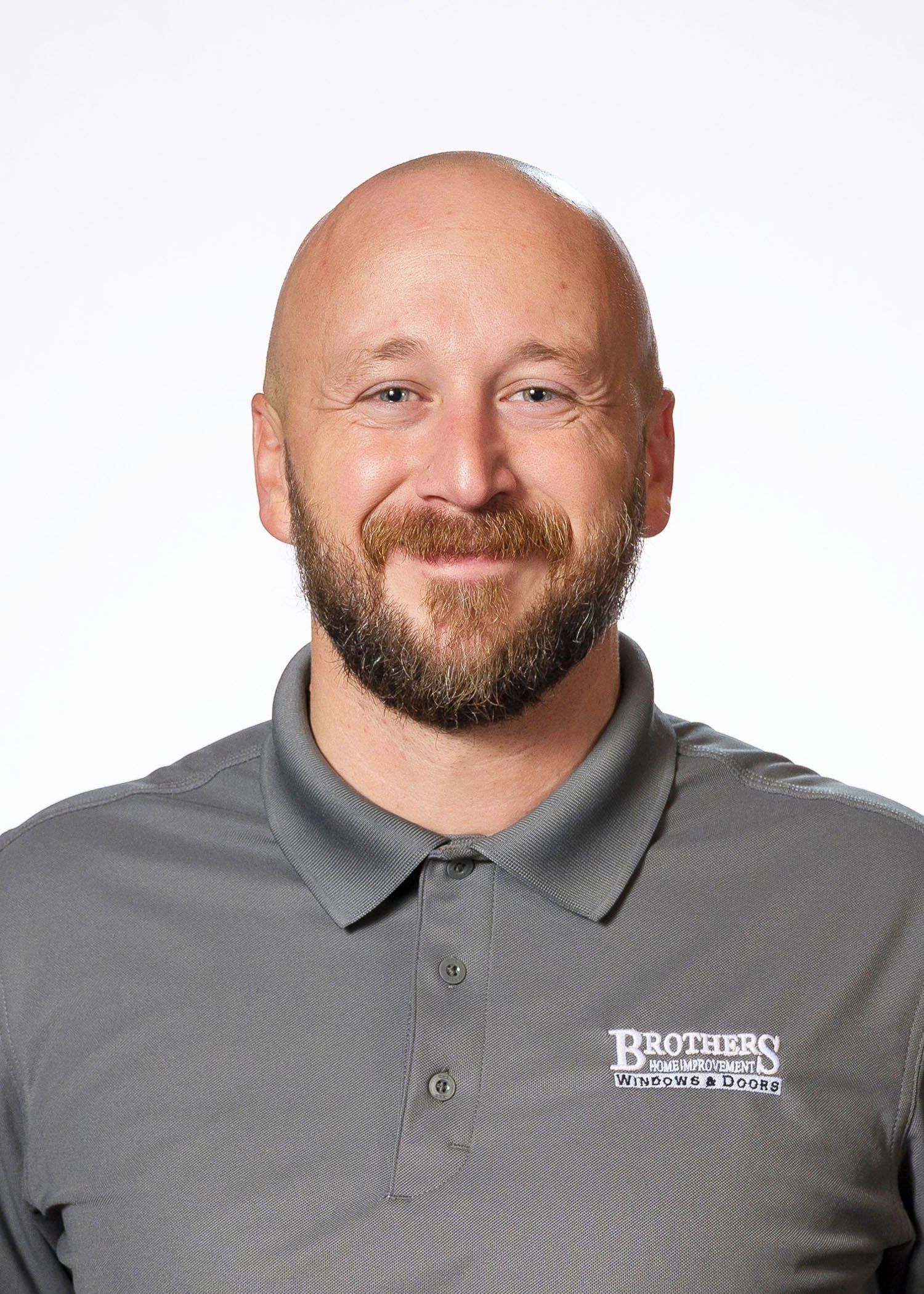 A bald man with a beard and mustache is wearing a gray polo shirt.