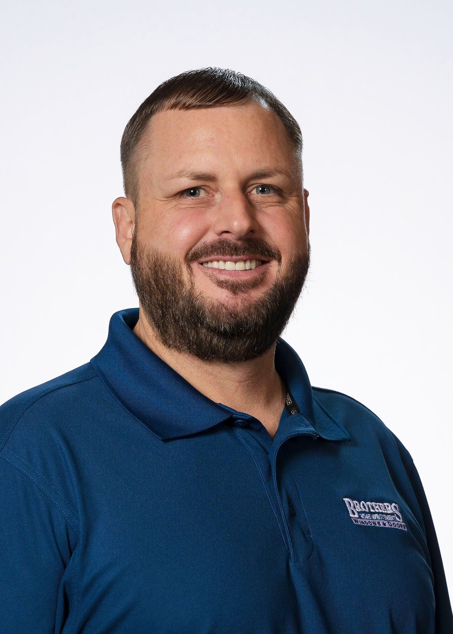 A man with a beard is wearing a blue shirt and smiling.