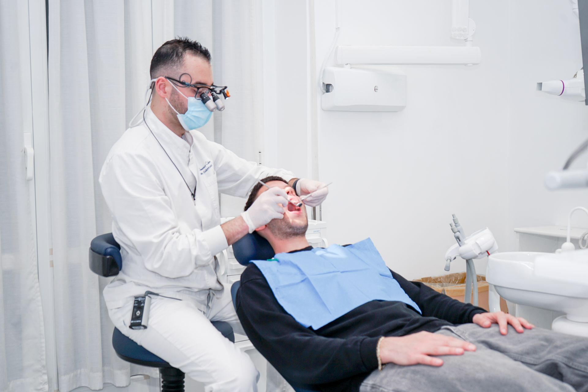 Un dentista con mascherina e lente d'ingrandimento esamina i denti di un paziente in un ambulatorio.