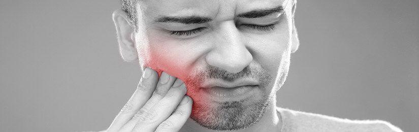 Una persona con un'espressione sofferente si tiene la mano sulla guancia, evidenziata in rosso per indicare un mal di denti.