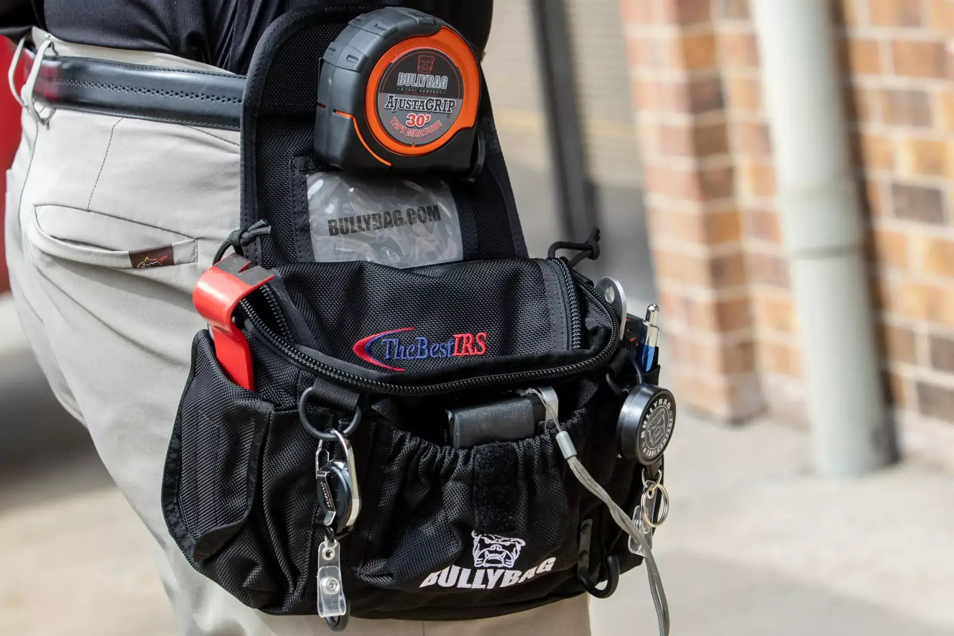 Black tool bag attached to a person's waist, containing tools and a tape measure.