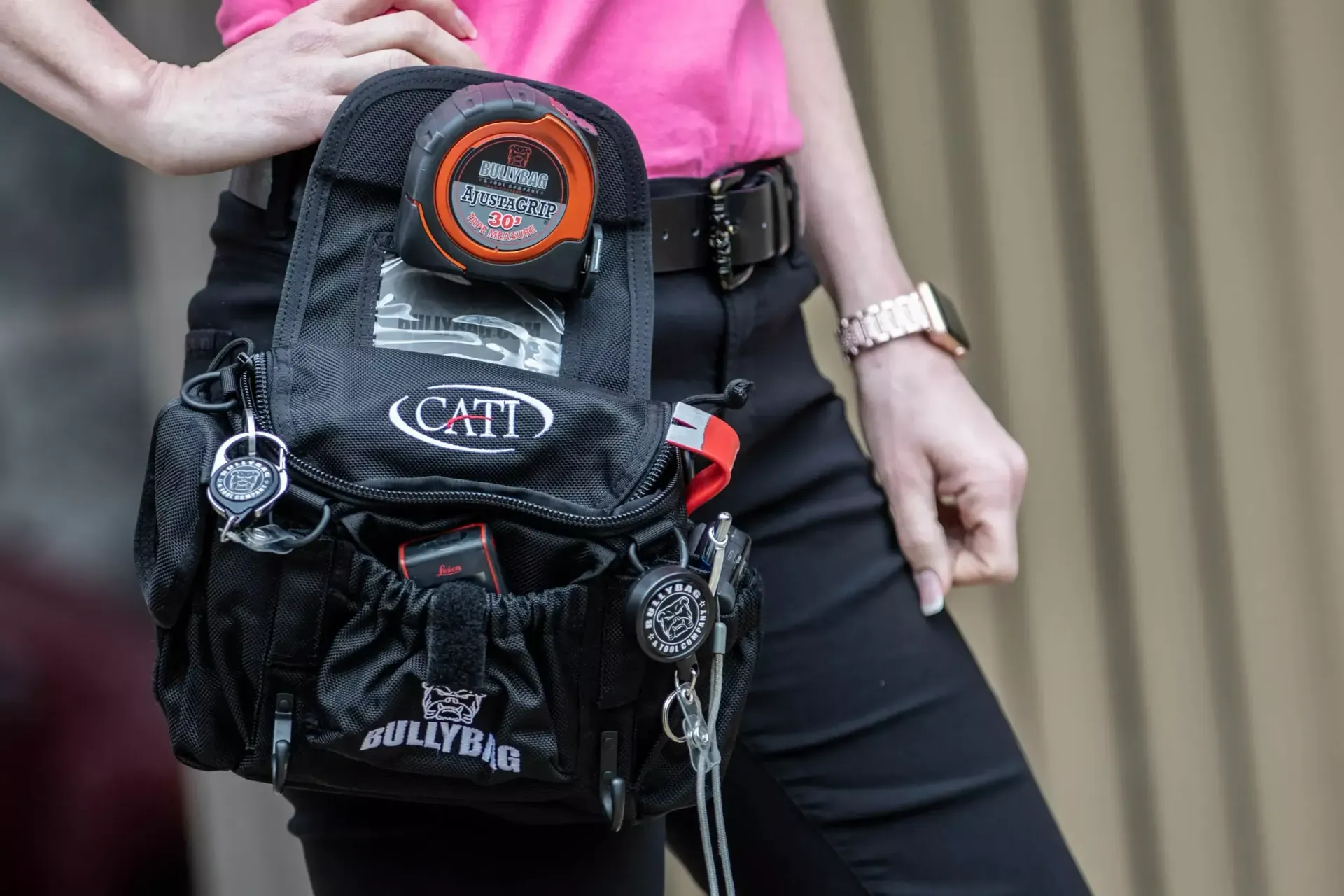 Person wearing a black tool belt, pink shirt, black pants, and a smart watch.