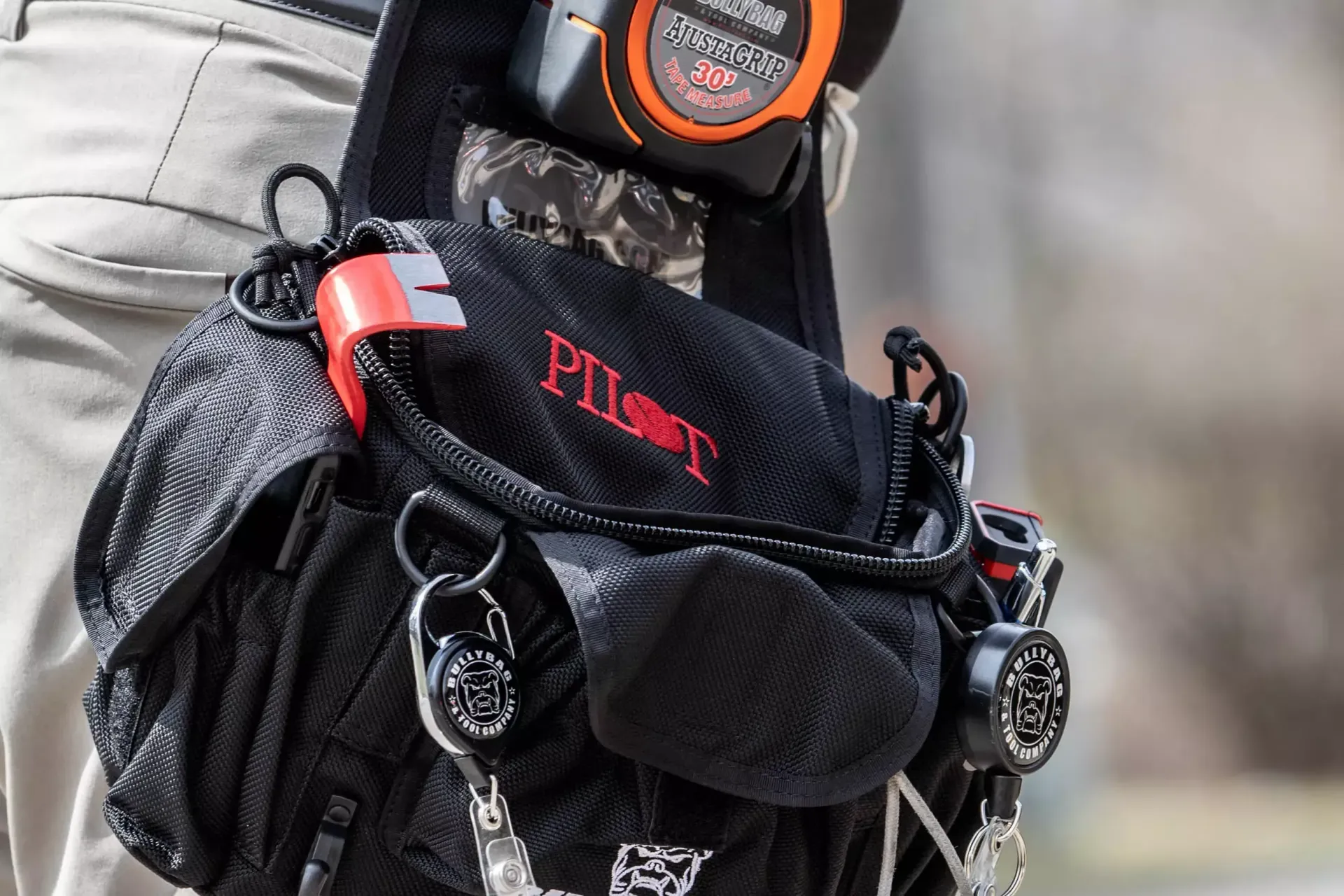 Black tool bag with red accents and logo on a person's belt, holding tools.
