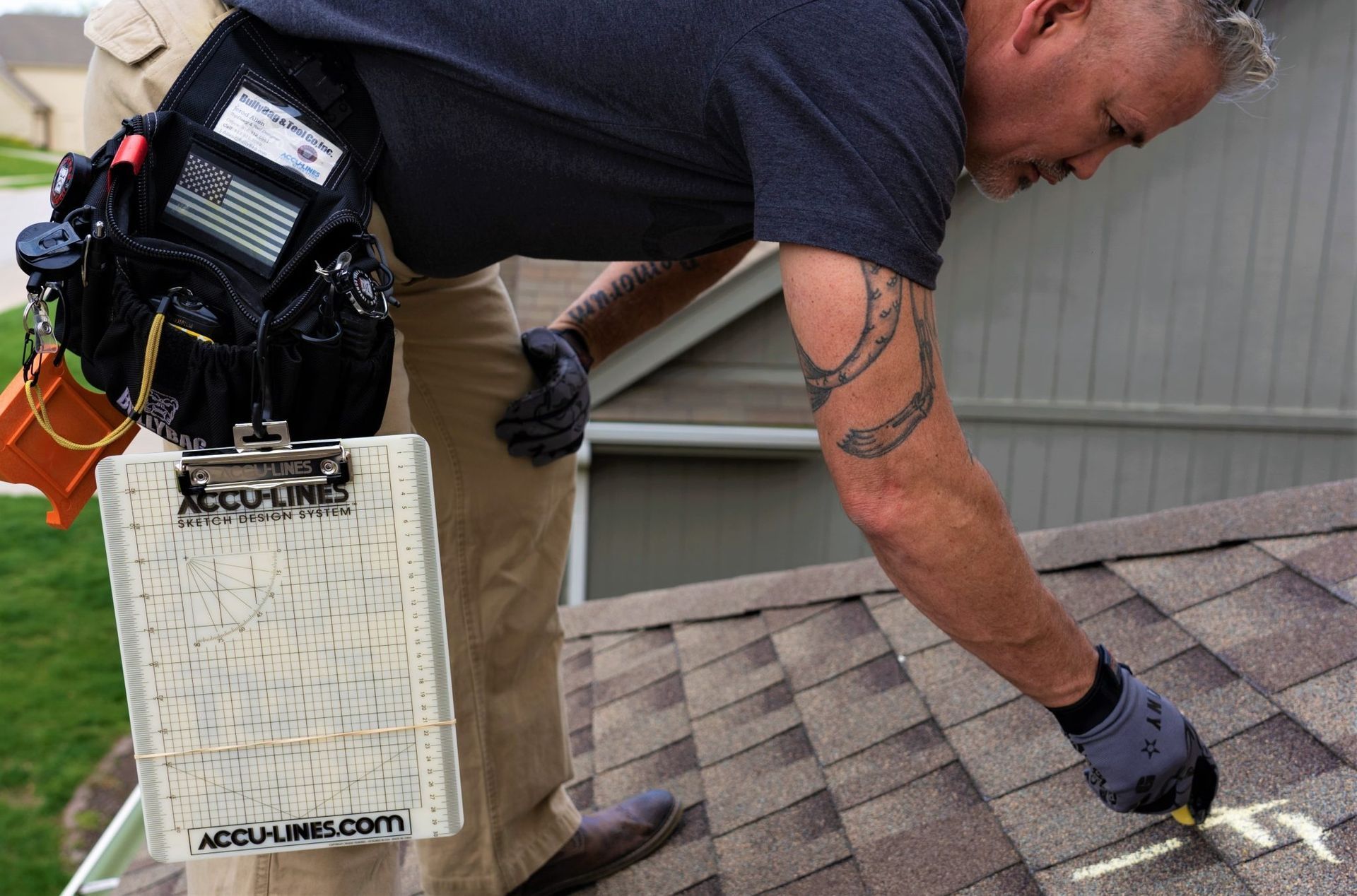 Roofer marking shingles with chalk on a residential roof, wearing a tool belt and gloves.