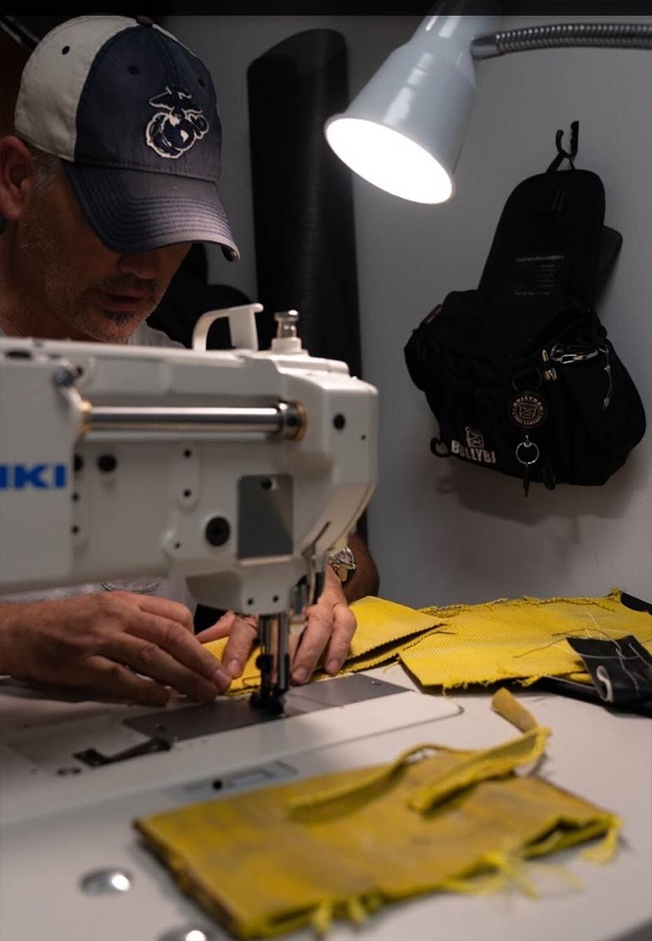 Person sewing yellow fabric with a white industrial machine under a lamp.