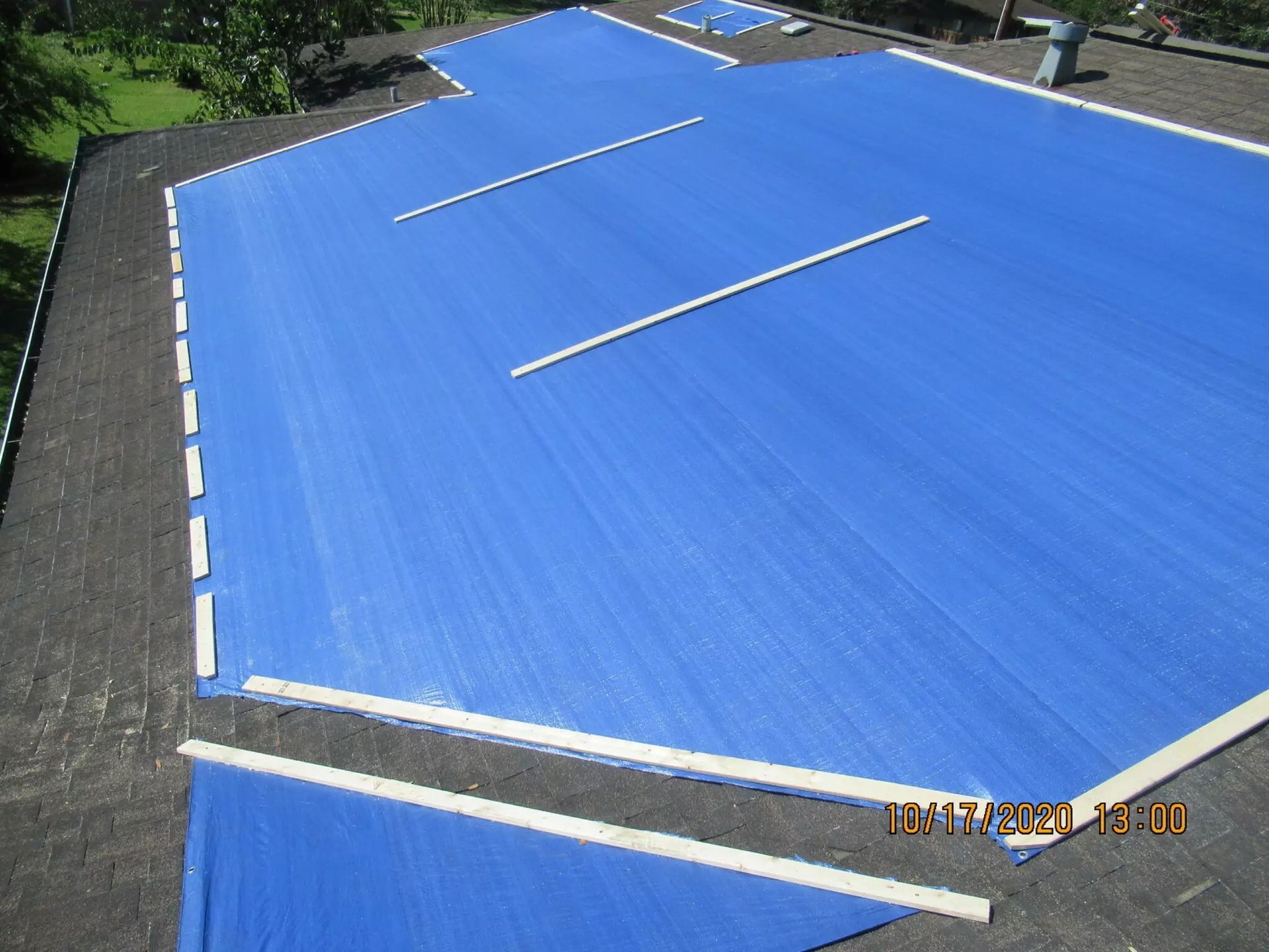 Blue tarp covering a flat roof, white wooden supports are on top.