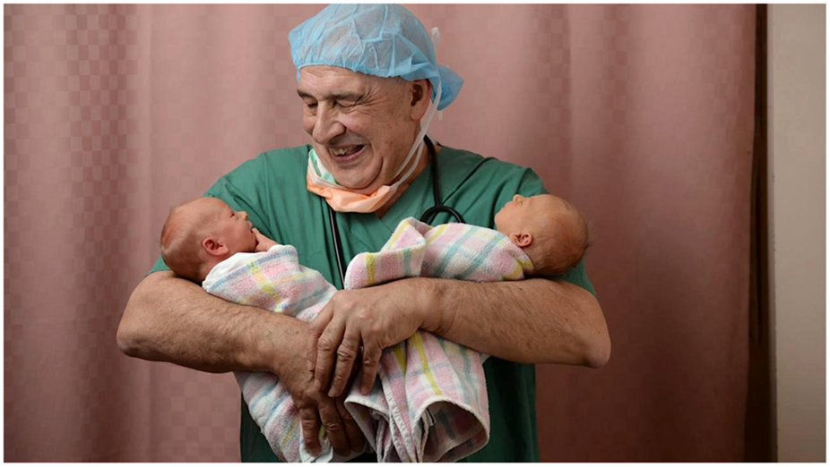 O&G specialist Dr John Svigos holding newborn twins, smiling in a hospital room.