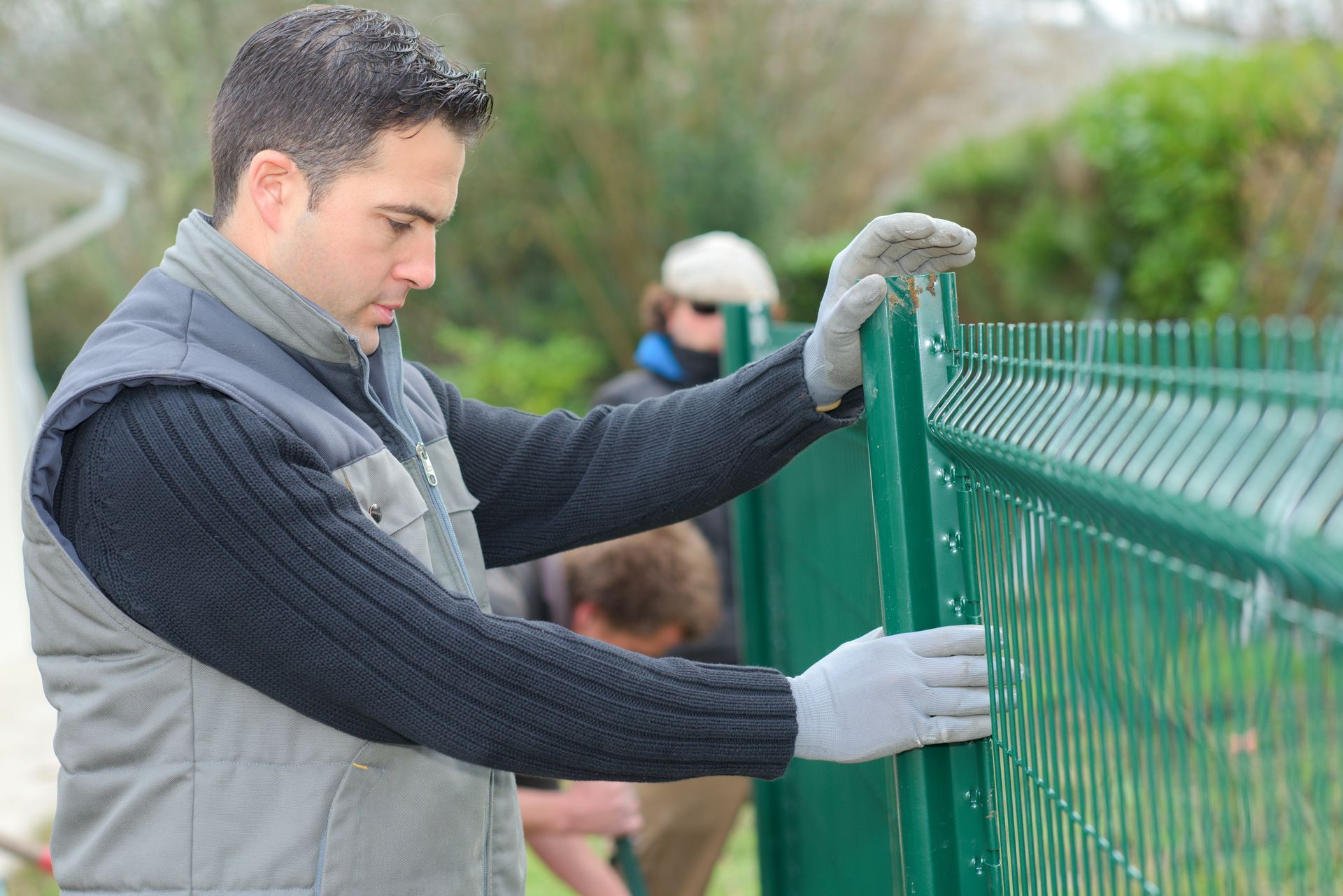 A man is standing next to a green fence.