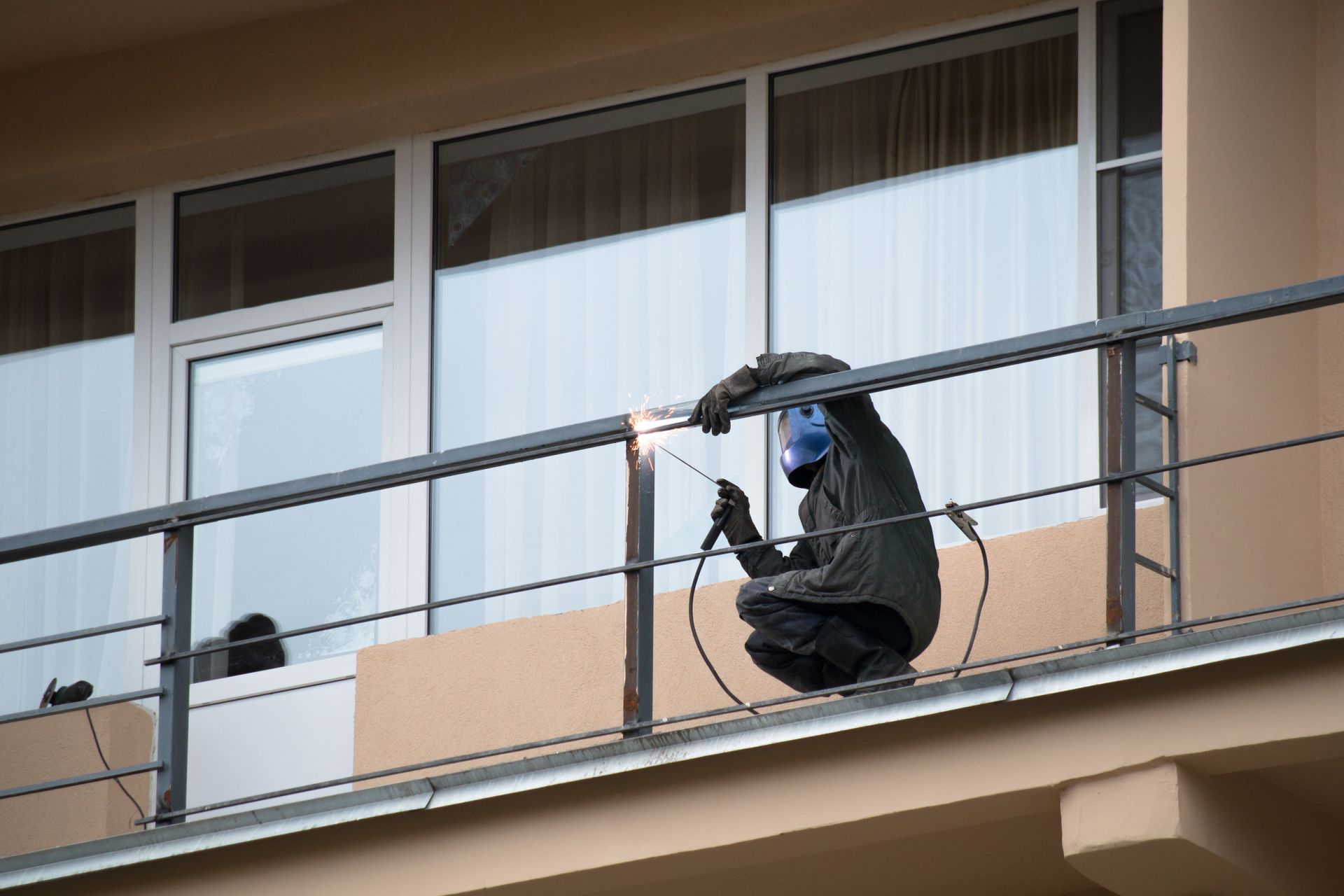 A man is welding a railing on a balcony.
