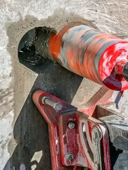 A red drill bit is being used to drill a hole in a wall.