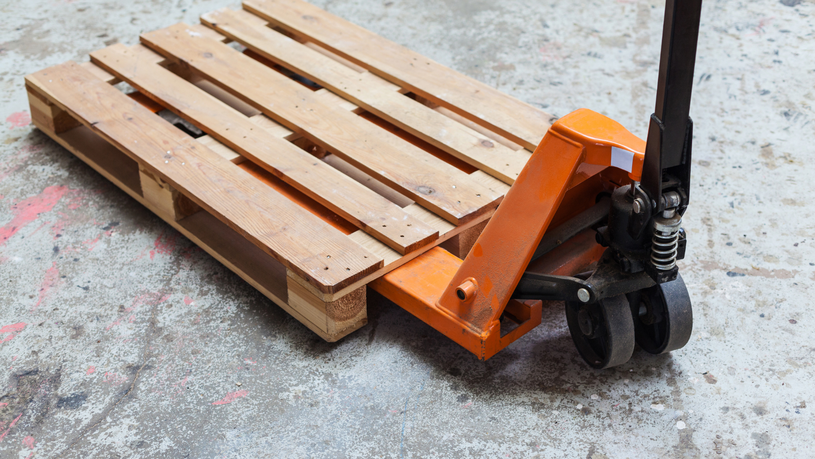 A wooden pallet is being pushed by a hand truck.