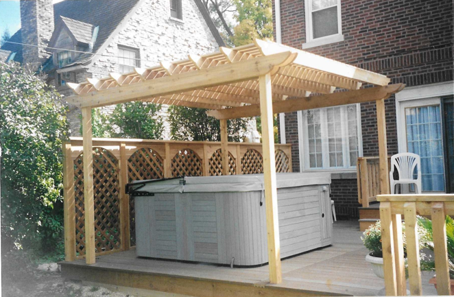A hot tub is under a wooden pergola on a deck