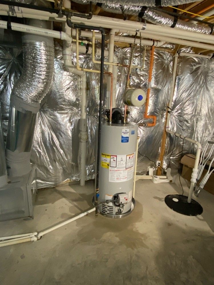 A water heater is sitting in a basement surrounded by pipes.