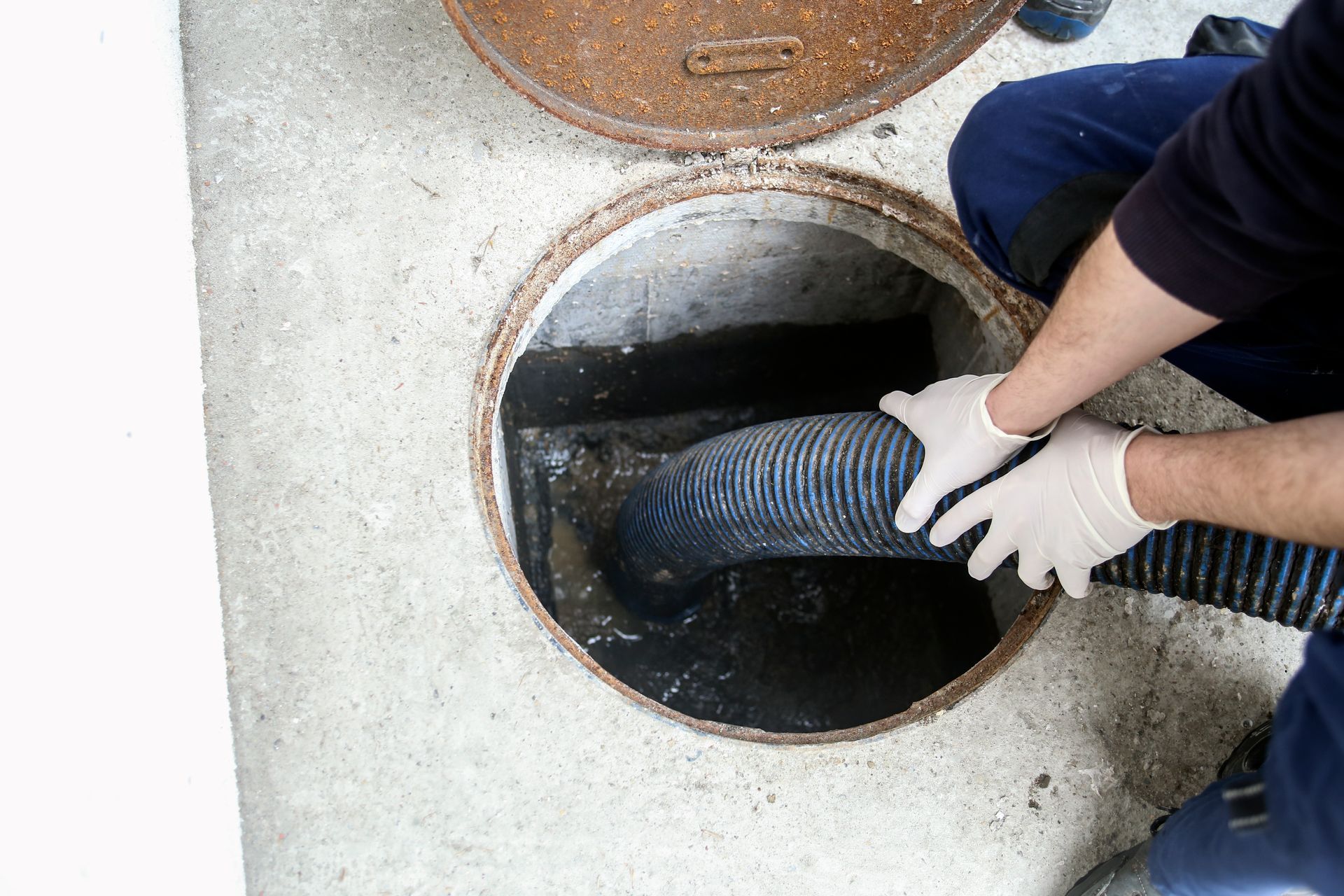 Two men are cleaning a manhole cover with a hose.