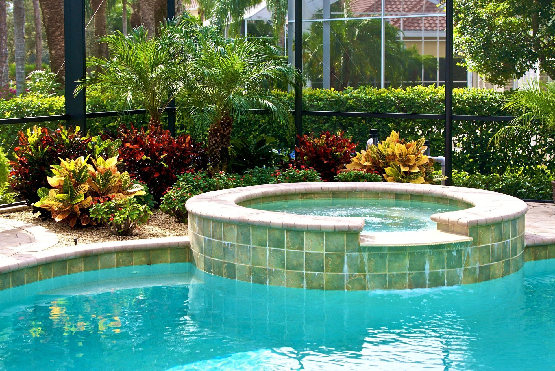 Backyard pool with a circular hot tub, turquoise water, and lush tropical landscaping