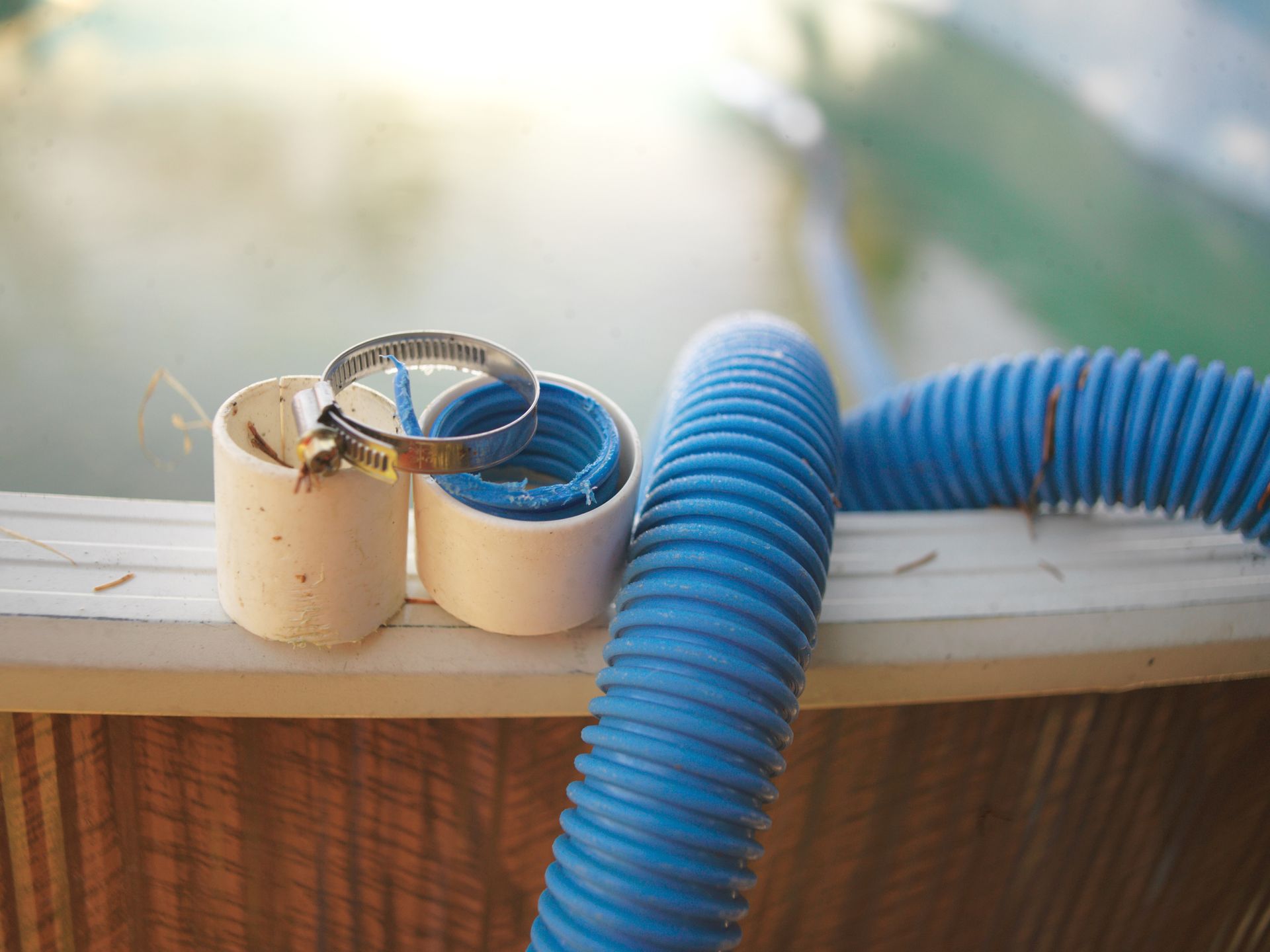 Two white PVC pipe segments and a blue corrugated hose with a metal clamp, resting on a wooden surface.