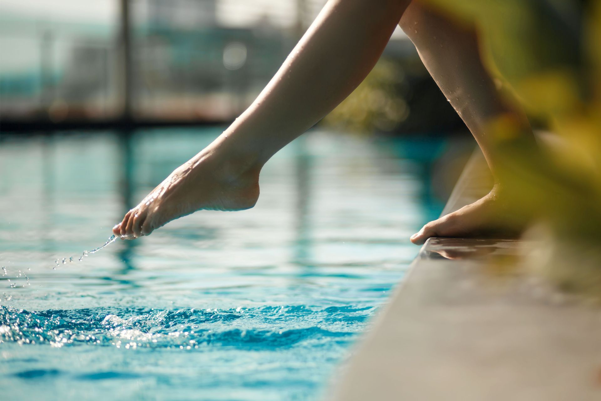 Feet dipping into a swimming pool beside the deck, with water splashing gently.