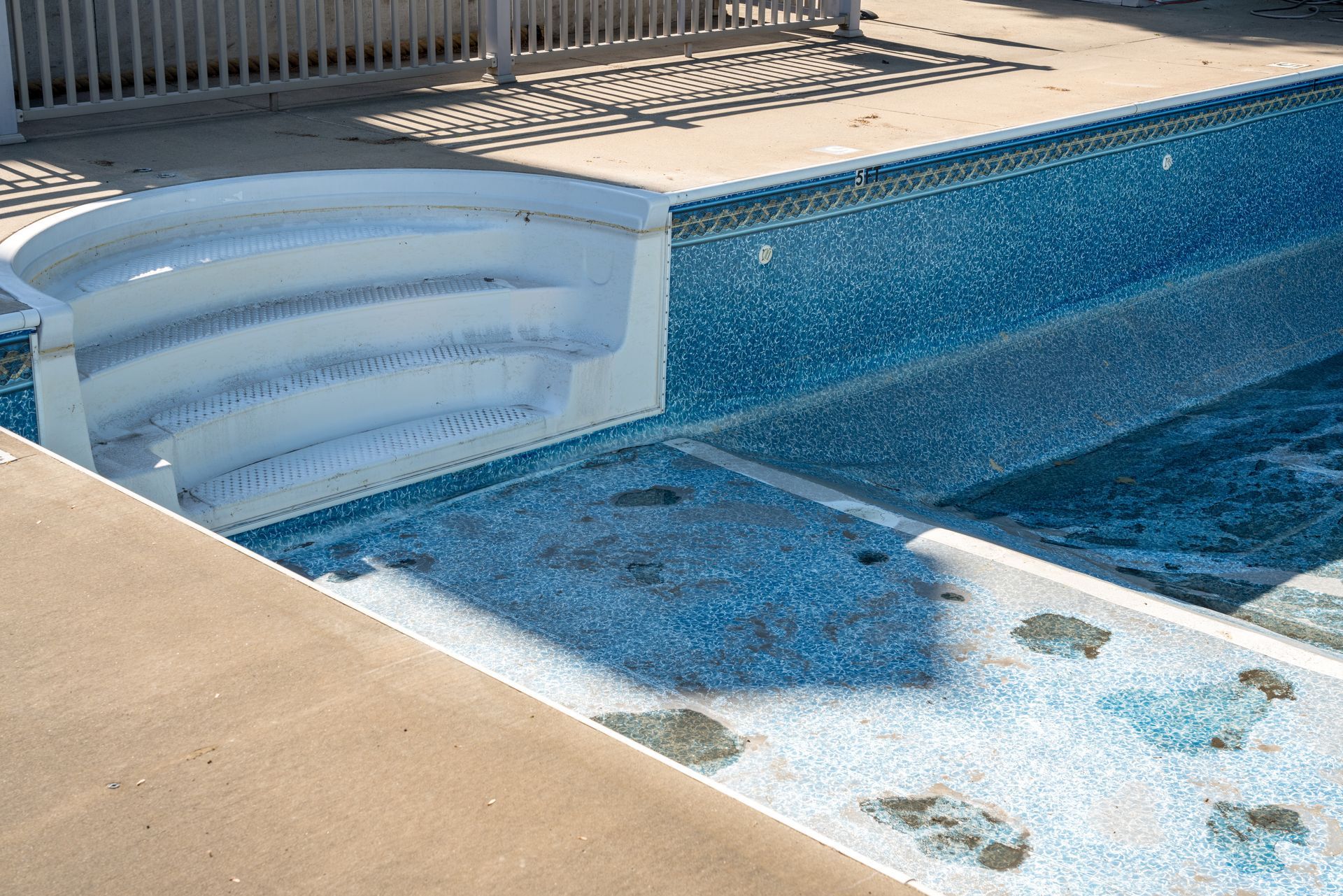 White built-in swimming pool steps lead into a shallow blue tiled area with a concrete deck surround.